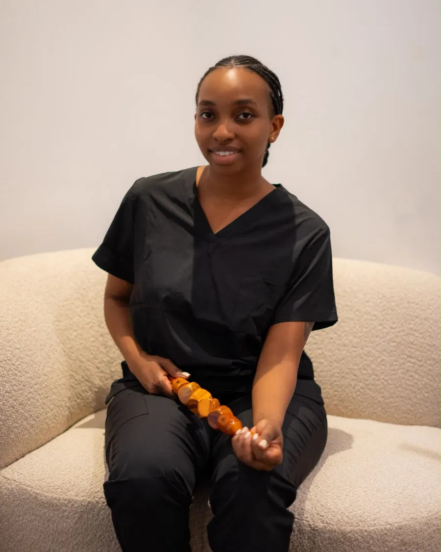 Gladys van Body Contour Clinic, zittend op de bank met een houten maderotherapie-instrument