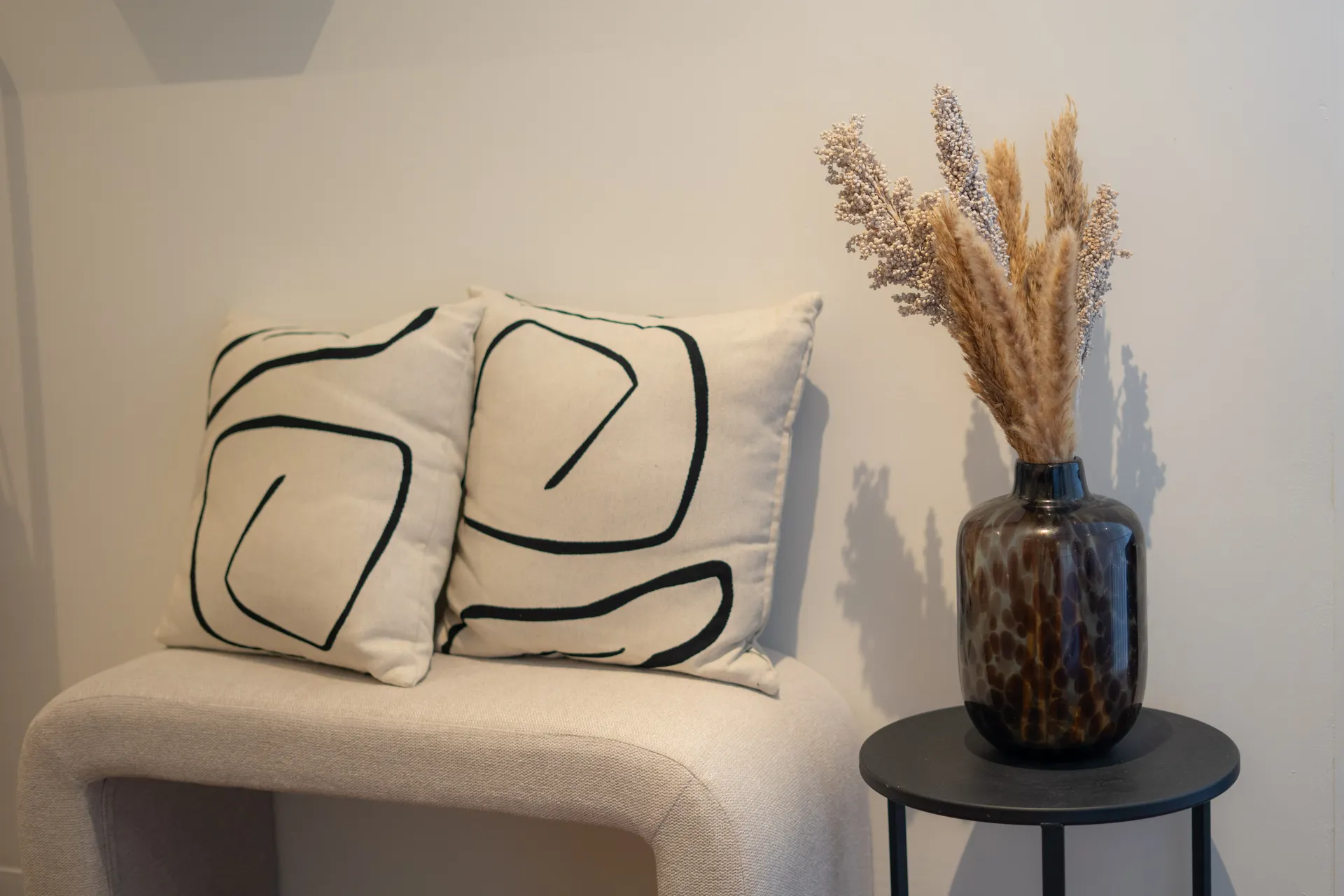 De lounge van Body Contour Clinic in Almere, met een zitbankje met kussens en gedroogde bloemen op een bijzettafel