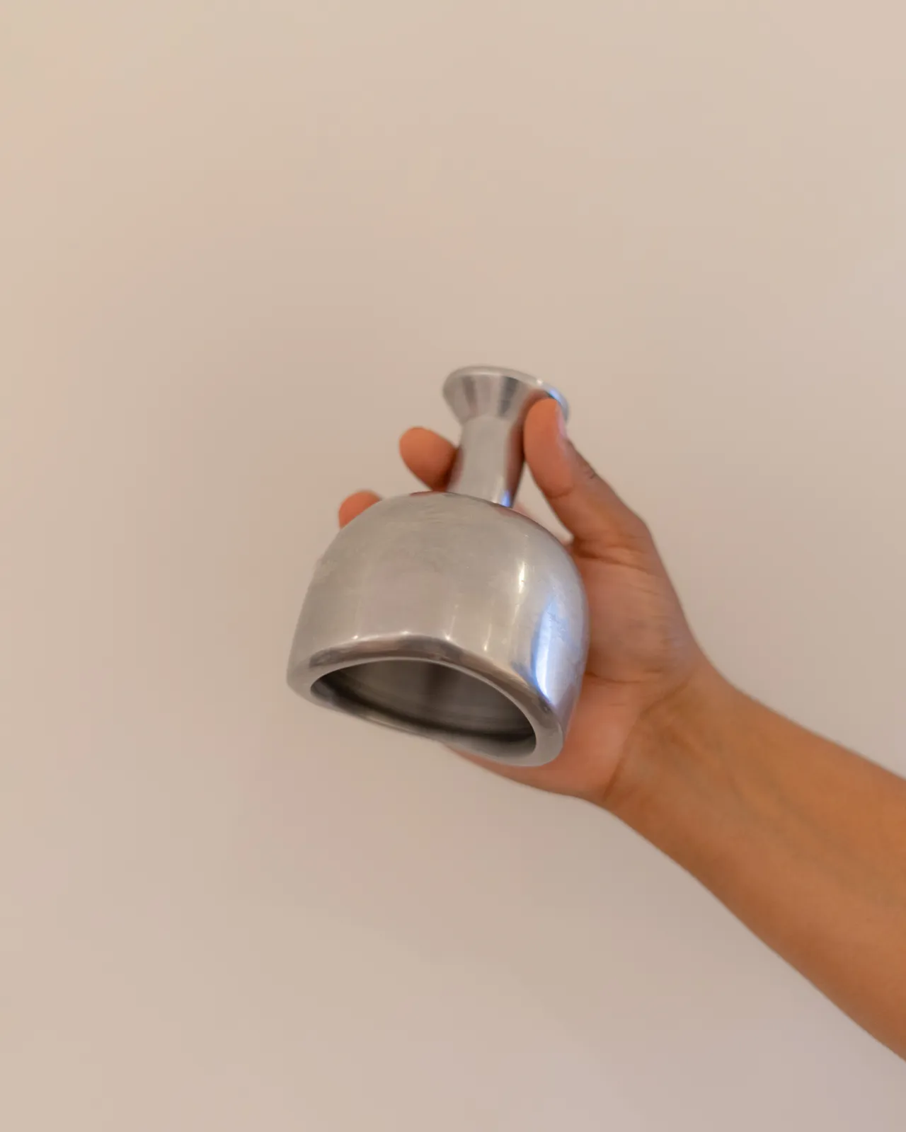 Hand met een metalen cupping-instrument tegen een rustige, lichte achtergrond